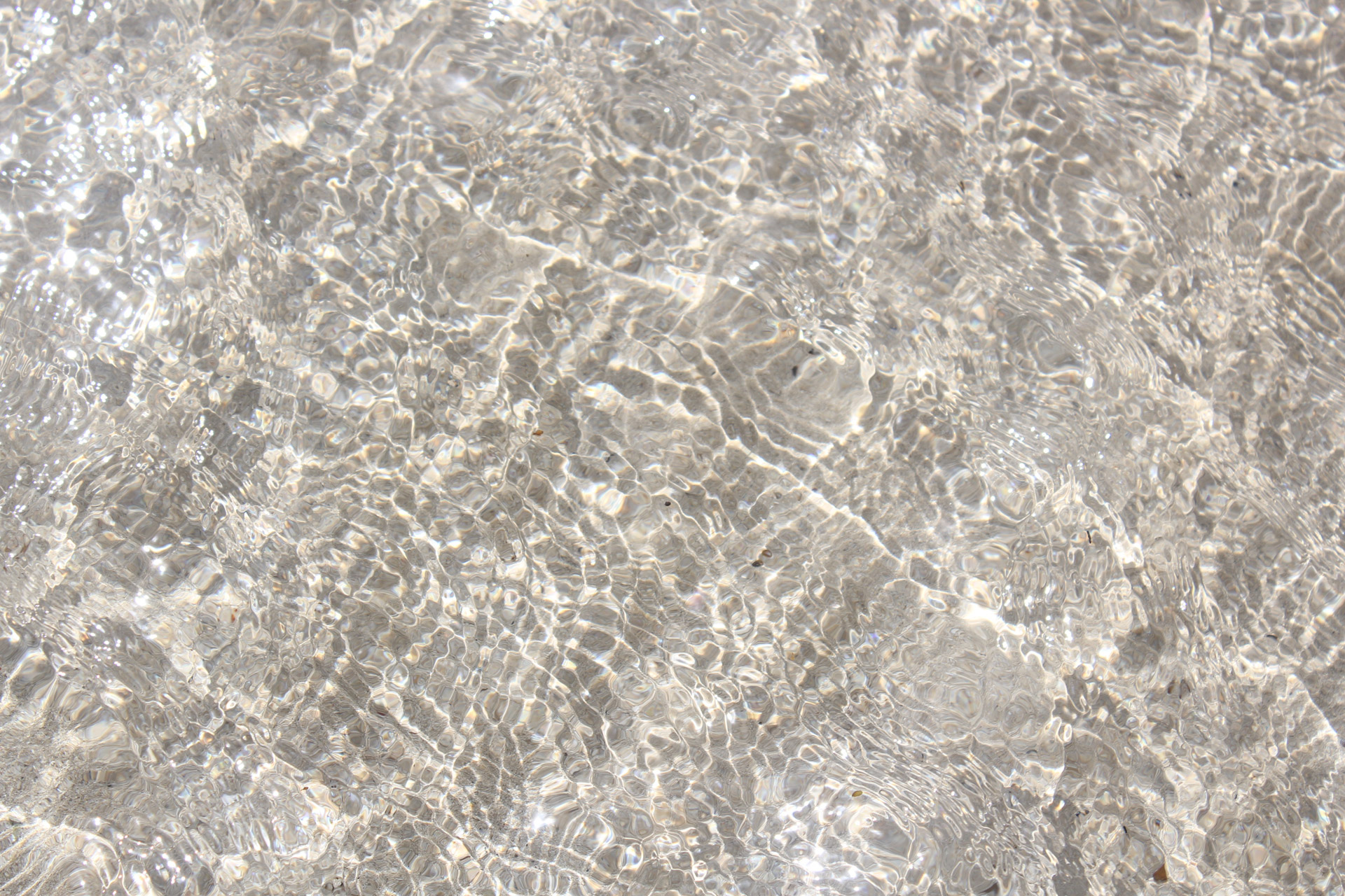 a closeup view of a crystal clear body of water with a light background beneath the surface. 
