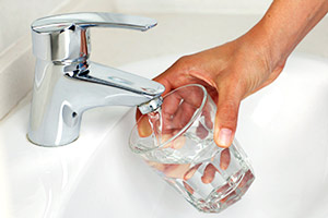 a person filling up a clear glass with tap water directly from the faucet. 